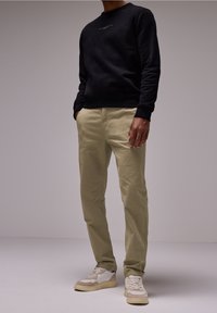 Black sweatshirt with a textured finish, paired with light khaki chinos. White and tan sneakers with a textured sole. Minimalistic design.
