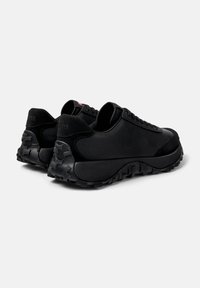 Black athletic shoes featuring a textured upper, sturdy rubber sole, and a unique tread pattern. Laces and branded accents in red.