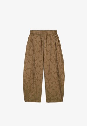 Lichtbruine loszittende broek met elastische tailleband en subtiel bladwijngrankarton door de stof heen.