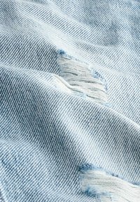 Vaaleansininen farkkukangas, jossa on pehmeä tekstuuri, frayed-patchit ja kuluneet alueet, jotka korostavat rentoa, kulunutta ilmettä.
