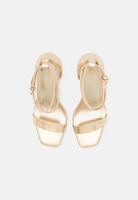 Guld metallic sandaler med firkantet tå og en bred rem over forsiden. En justerbar ankelrem har en lille spænde-detalje.