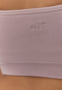 Reggiseno sportivo viola chiaro a coste con texture morbida, caratterizzato da un logo in rilievo "selfi" sul davanti e una fascia senza cuciture per il massimo comfort.
