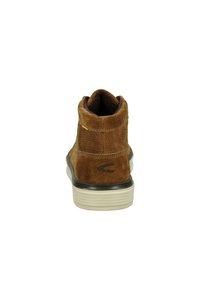 Brown suede ankle boot with a rounded toe, textured panels, and a contrasting white rubber sole. Features a prominent logo on the heel.