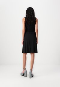 Top negru fără mâneci cu un design strâns, asortat cu o fustă neagră evazată. Modelul poartă tocuri gri cu platformă și curele la glezne.