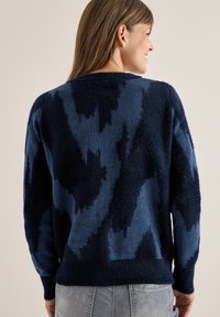 Navyblauer Pullover mit einer weichen, flauschigen Textur, der ein wirbelndes Muster und einen gerippten Saum aufweist. Überdimensionierte Passform mit überschnittenen Schultern.