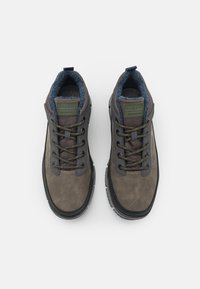 Hnědé a šedé šněrovací boty s texturovaným svrškem, měkkým límcem a gumovou podrážkou, s zelenou nášivkou na jazyku.