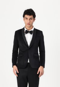Jachetă de tuxedo neagră cu reveruri din satin, �închidere cu un singur nasture și două buzunare frontale. Purtată peste o cămașă albă și o cravată papion neagră.