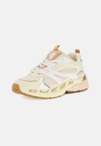 Zapatillas deportivas voluminosas en crema y beige, con superposiciones de malla y sintéticas, suela texturizada y logotipo en el lateral.