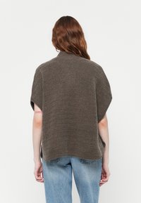 Pruunist kudumist pullover, millel on lühikesed varrukad, tekstuuriga kangas ja kõrge kaelus. Laineline istuvus külgsuistega, koos helesiniste teksadega.