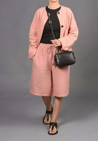 Chaqueta de lino rosa claro sobre una blusa negra, combinada con pantalones cortos rosa claro y sandalias negras. Pequeño bolso cruzado negro con detalles en metal.