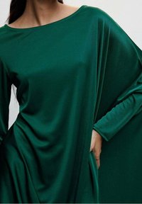 Grünes, fließendes Kleid aus glattem Stoff mit weitem Bootsausschnitt und lockeren Ärmeln. Es hat eine lässige Passform und einen eleganten Fall.