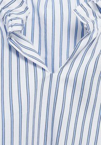 Striped blouse featuring a light blue and white color scheme, made of soft cotton fabric with a V-neckline and ruffled accents.