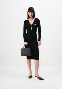 Black ribbed dress with a V-neck and gold button accents, paired with a black structured handbag featuring an embossed design and short handles.