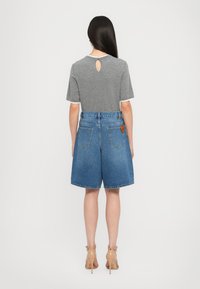 Top corto gris de manga corta con un detalle de ojal en la parte posterior, combinado con pantalones cortos de mezclilla azul claro que cuentan con dos bolsillos traseros y un acento de etiqueta marrón.