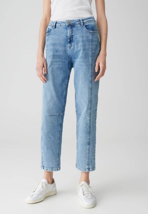 Lichtblauwe denim jeans met een recht gesneden pijp, vijf zakken en een subtiele vervaagde textuur, gecombineerd met witte sneakers.