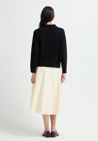 Schwarzer Pullover mit Kragen, kombiniert mit einem cremefarbenen Midirock. Das Outfit hat eine lockere Passform und eine glatte Textur. Dunkle Schuhe runden das Gesamtbild ab.