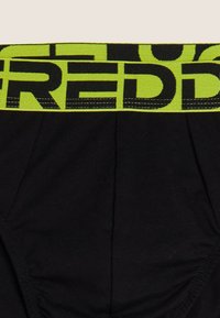 Slip in cotone nero con elastico in vita verde brillante e testo nero audace. Il design presenta dettagli sottili di trama e cuciture.