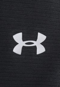 Czarna tkanina o teksturze z wyraźnym białym logo Under Armour. Projekt jest prosty, z gładkimi, zaokrąglonymi brzegami i minimalnymi detalami.
