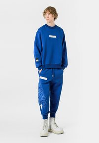 Sudadera azul y pantalones a juego hechos de una mezcla de algodón, con un diseño de alas bordado, acentos blancos y bolsillos laterales.