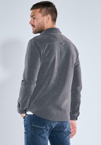 Gray corduroy shirt with a rear yoke, buttoned cuffs, and side slits, shown with denim jeans against a light background.