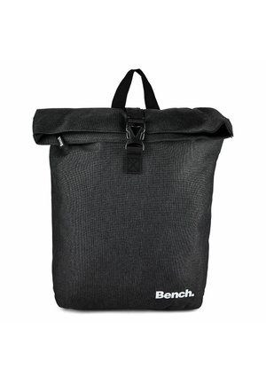 Sac à dos en tissu noir à rabat roulé avec une sangle à boucle à l'avant, une poignée de transport et le logo blanc "Bench." en bas à droite.