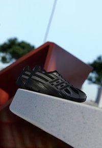 Čierne športové topánky s hornej časťou z mäkkej sieťoviny, syntetickými prekrytiami a textúrovanou podrážkou. Obsahujú reflexné akcenty a elegantný, aerodynamický dizajn.