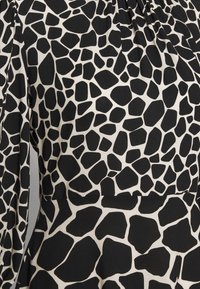 Svart och vit klänning med ett texturerat, abstrakt mönster som påminner om djurfläckar. Tyget är mjukt med en slät yta.