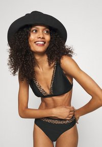 Svart bikini med leopardmønster på kantene, som har en trekantet topp og matchende høyt liv-bunn; glatt tekstur.