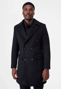 Svart dubbelknäppt kappa i en ullblandning. Har stora knappar, markerade slag och två framfickor. Slät textur.