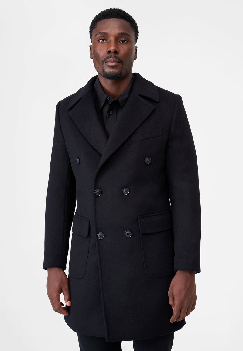 Svart dubbelknäppt kappa i en ullblandning. Har stora knappar, markerade slag och två framfickor. Slät textur.