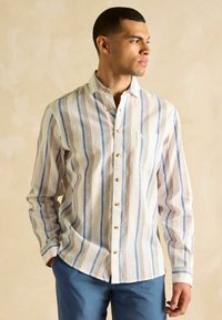 Ribadeetud nööpidega särk, millel on valge tausta peal sinised, rohelised ja roosad triibud. Särgil on rinna küljes tasku ja kuldsed nööbid.