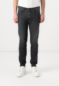 Jeans negre închis cu o croială slim, având buzunare frontale, închidere cu nasture și detalii de cusătură subtile. Purtați cu adidași albi.
