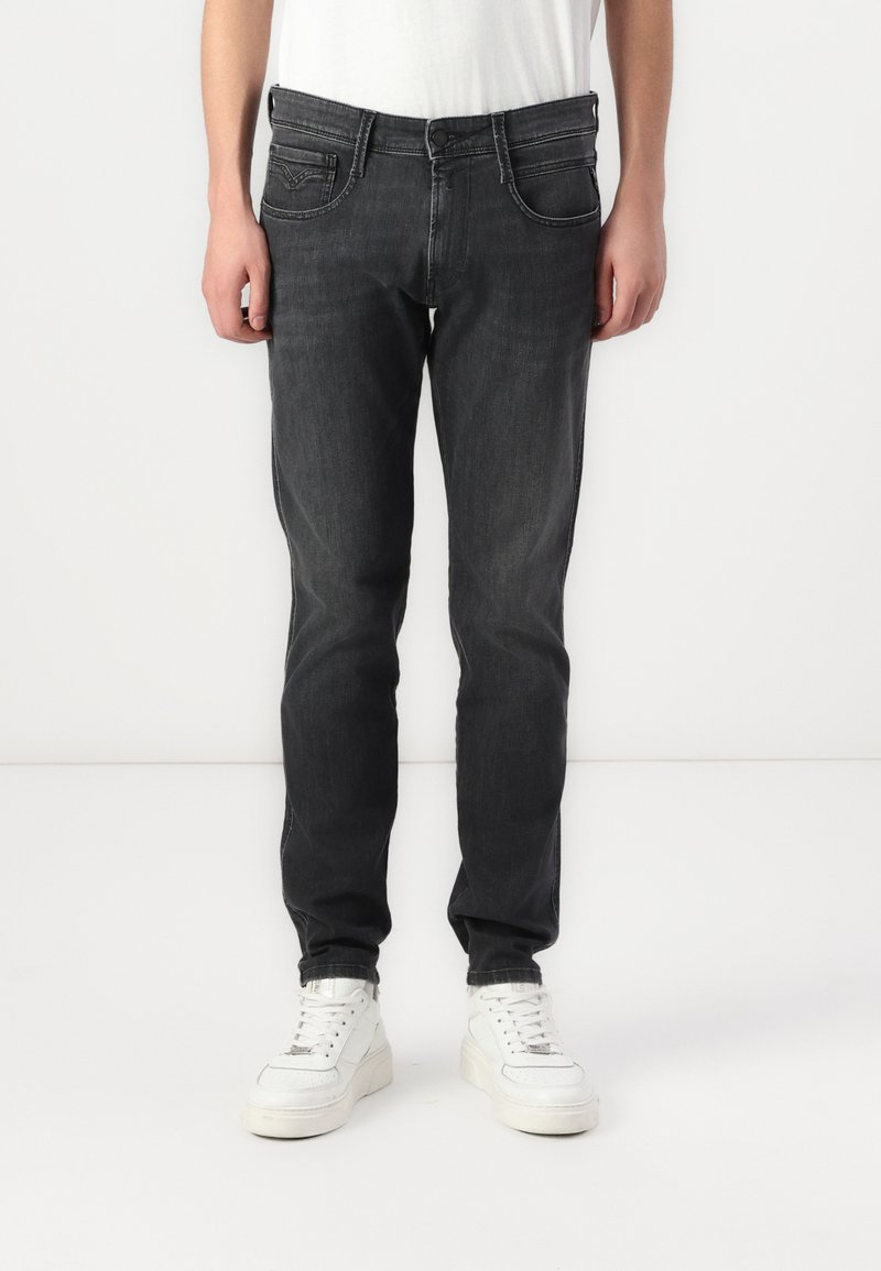 Jeans negre închis cu o croială slim, având buzunare frontale, închidere cu nasture și detalii de cusătură subtile. Purtați cu adidași albi.