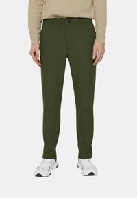 Pantaloni slim-fit verde oliva con una texture liscia, vita elastica, chiusura con bottone e tasche frontali, abbinati a scarpe da ginnastica bianche.