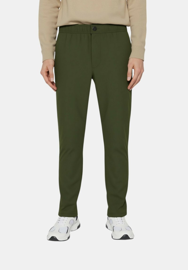 Pantaloni slim-fit verde oliva con una texture liscia, vita elastica, chiusura con bottone e tasche frontali, abbinati a scarpe da ginnastica bianche.