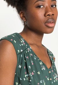 Blusa verde com estampa de borboletas multicoloridas, tecido leve, decote em V e detalhes em botão na frente. Apresenta mangas curtas e textura suave.