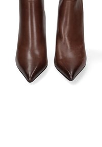 Bottines en cuir marron avec embouts pointus, texture lisse et talons aiguilles hauts. Aucun matériel ou motif visible.
