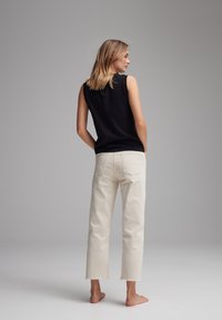Top senza maniche nero abbinato a jeans cropped color crema. I jeans presentano un orlo sfilacciato e tasche posteriori, evidenziando un look informale.