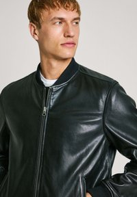 Juodas odinis bomber tipo švarkas su užtrauktuku, ribotu apykakle ir tekstūruotu paviršiumi. Yra dvi šoninės kišenės ir elegantiškas siluetas.