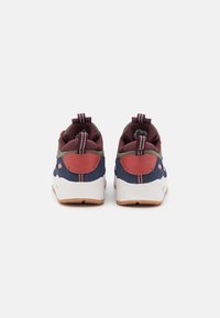 Vista posteriore di sneakers con materiali in blu navy, bordeaux e verde oliva, una suola bianca, dettagli rossi e doppi tiranti.