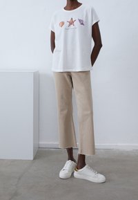 Vit bomulls t-shirt med broderade snäckdesigns. Matchad med beige avkortade byxor och vita sneakers med guldaccenter.