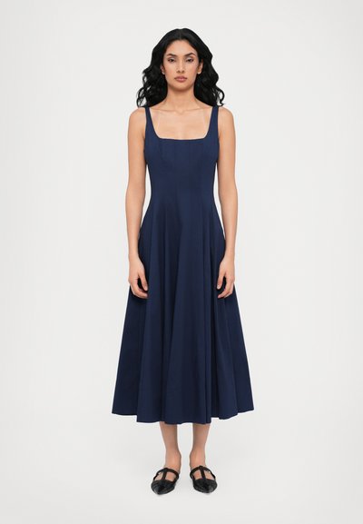 Navyblauw mouwloos jurk met een vierkante halslijn, vloeiende A-lijn rok en gestructureerde stof; gecombineerd met zwarte platte schoenen.