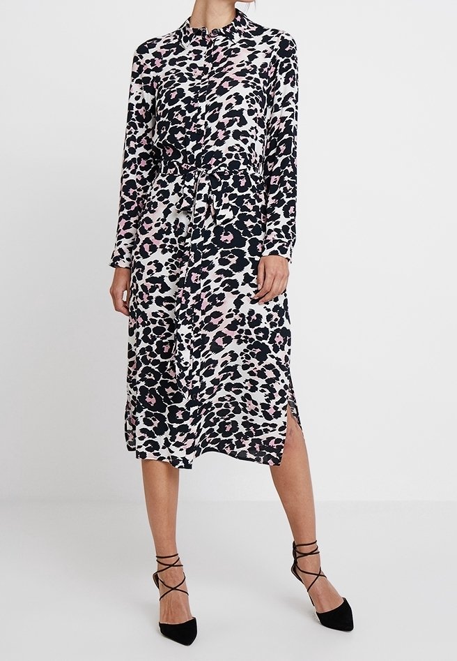 Femme portant une robe midi à manches longues boutonnée avec un imprimé léopard rose et noir et des talons noirs à lacets.