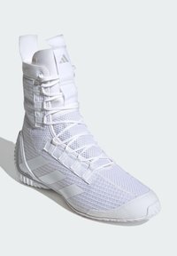 Zapatilla deportiva alta blanca con parte superior de malla texturizada, sistema de cordones prominente, suela de goma y tres rayas diagonales en el lateral.