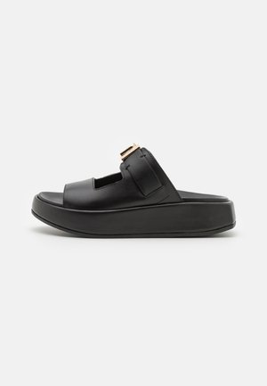Sandalia tipo slider de cuero negro con tira ancha ajustable y hebilla dorada, con suela gruesa de plataforma.