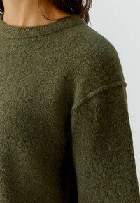 Olivgrüner Pullover aus weichem, strukturiertem Stoff. Verfügt über einen gerippten Halsausschnitt und überschnittene Schulternähte für eine lockere Passform.