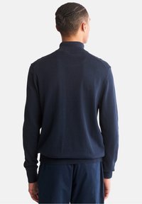 Suéter de punto azul marino con cuello alto, mangas largas y puños y dobladillo acanalados. Textura suave con mínimos detalles de costura.
