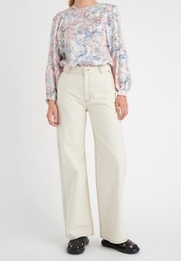 Pantaloni bianchi a gamba larga con cuciture a contrasto abbinati a una blusa leggera a fantasia floreale in morbidi colori pastello. Sandali neri senza chiusura.