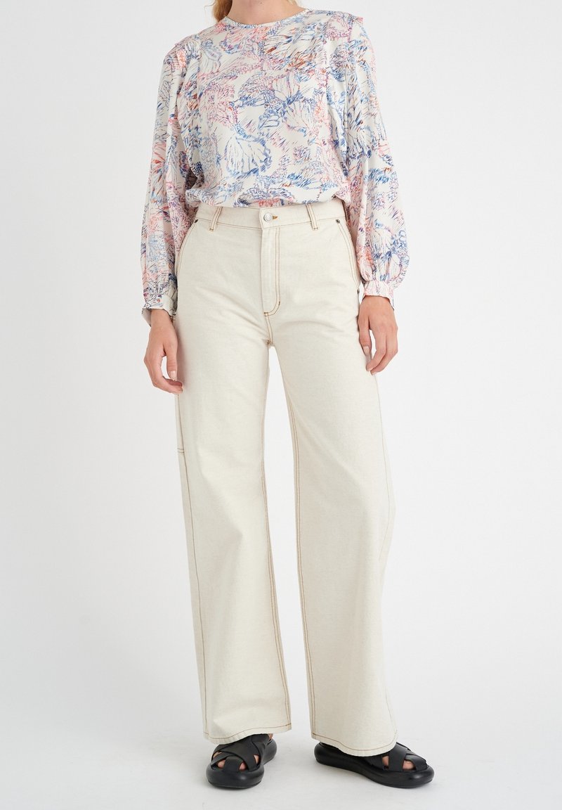 Pantaloni bianchi a gamba larga con cuciture a contrasto abbinati a una blusa leggera a fantasia floreale in morbidi colori pastello. Sandali neri senza chiusura.