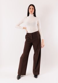 Maglione a collo alto beige con trama a coste, abbinato a pantaloni marroni a vita alta e gamba larga, e décolleté nere con punta appuntita.